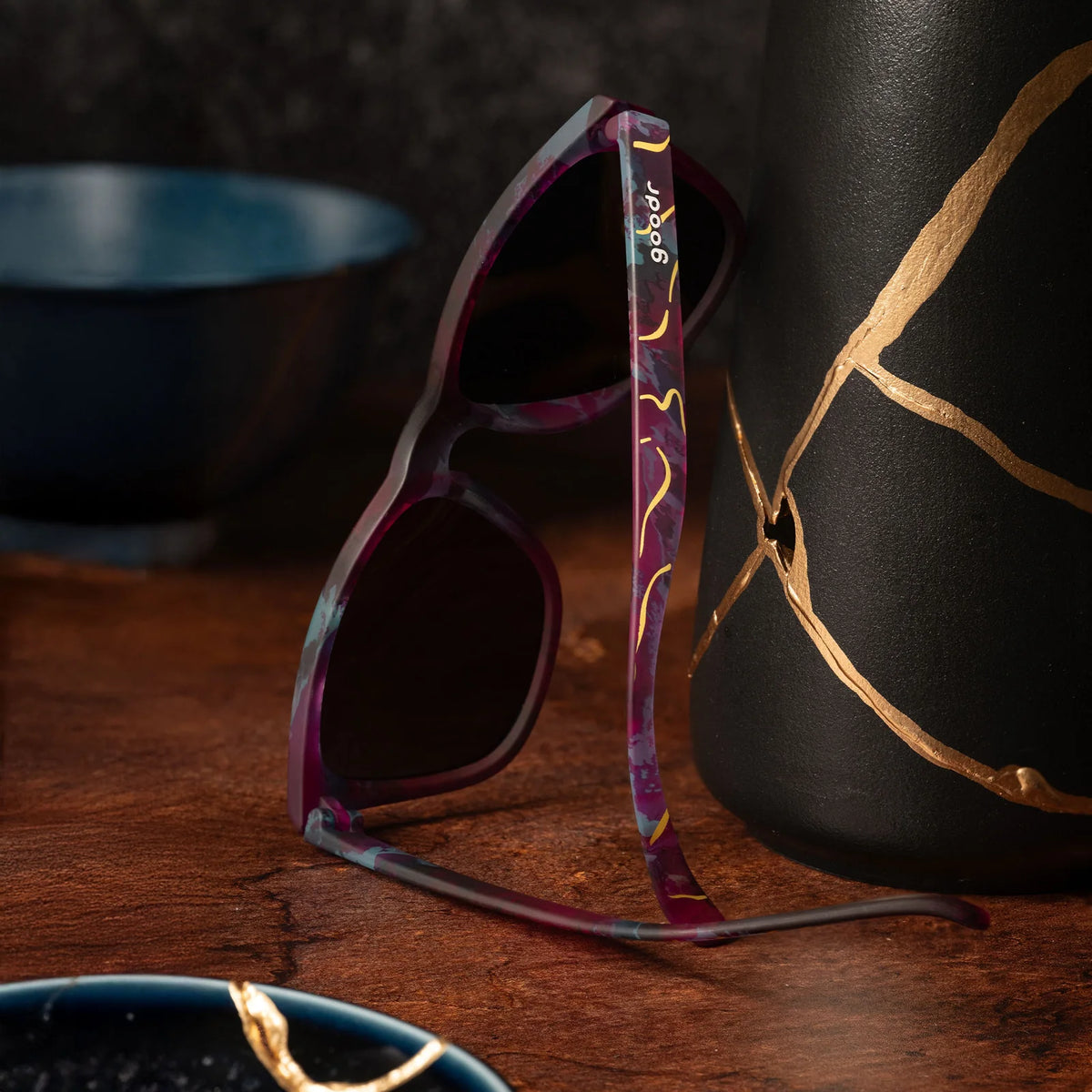 Multi-coloured sunglasses with a prominent gold line pattern. Pinks, purples, and blues on these square-shaped frames.